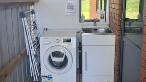A compact laundry area with a washing machine, a dryer, and a sink. - Rural cottage        (Tuamarina)