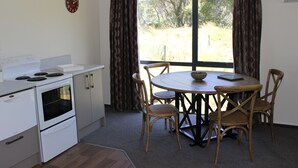 A compact kitchen with a stove, oven, and a dining table with chairs. - Rural cottage        (Tuamarina)