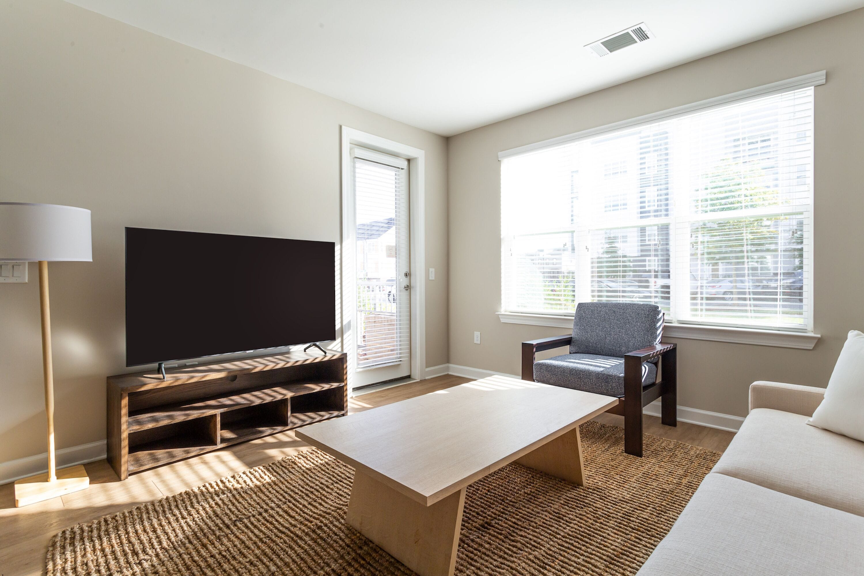 Un salon avec un téléviseur à écran plat posé sur un meuble en bois, un canapé, un fauteuil et une table basse.