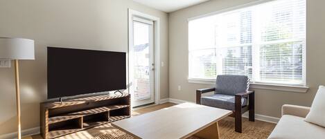 Un salon avec un téléviseur à écran plat posé sur un meuble en bois, un canapé, un fauteuil et une table basse.