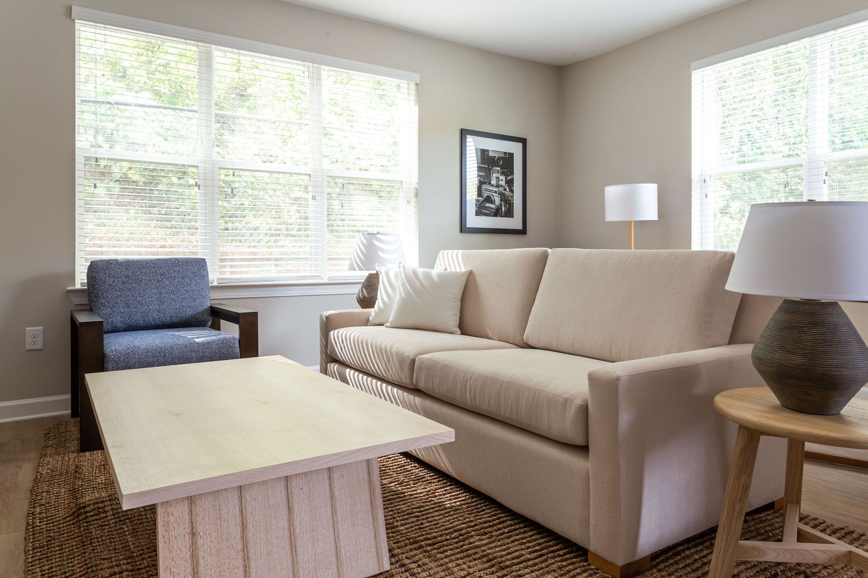 A living room with a beige sofa, a blue armchair, a wooden coffee table, and a lamp on a side table.