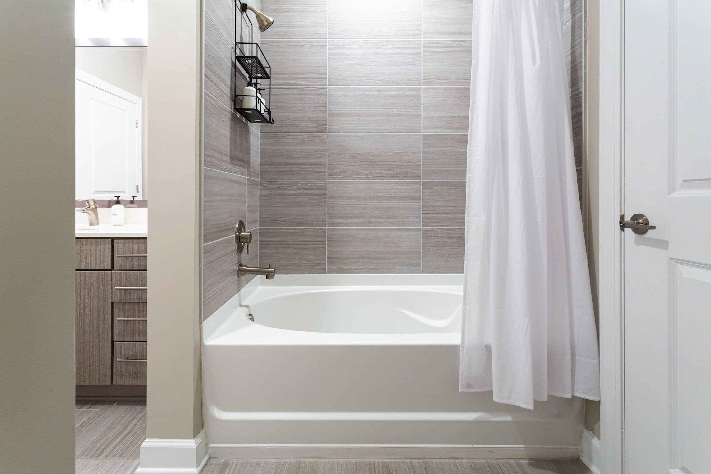 A modern bathroom with a bathtub, a shower curtain, and a wooden cabinet.