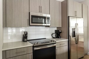 A modern kitchen with light wood cabinets, a stainless steel microwave, a refrigerator, and a built-in oven.