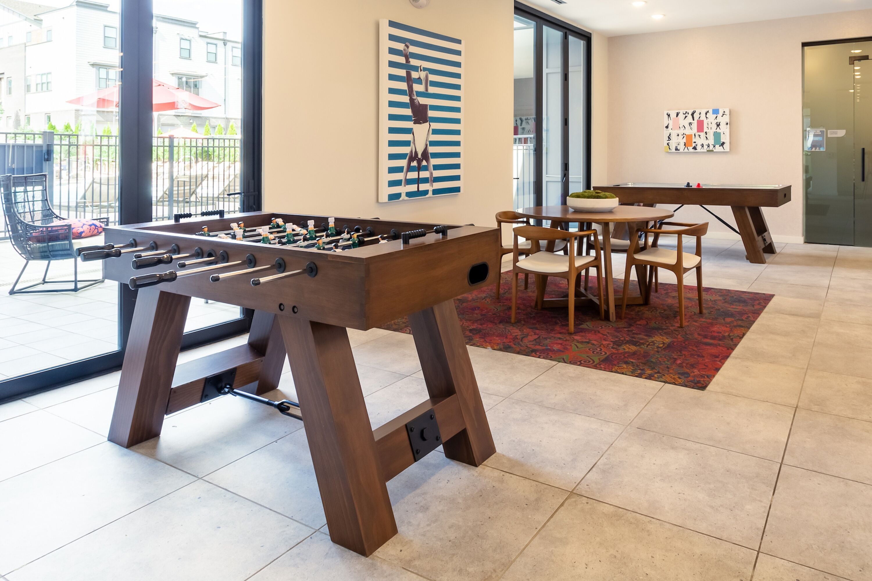 A room with a foosball table, a pool table, and a dining area with chairs and a table.