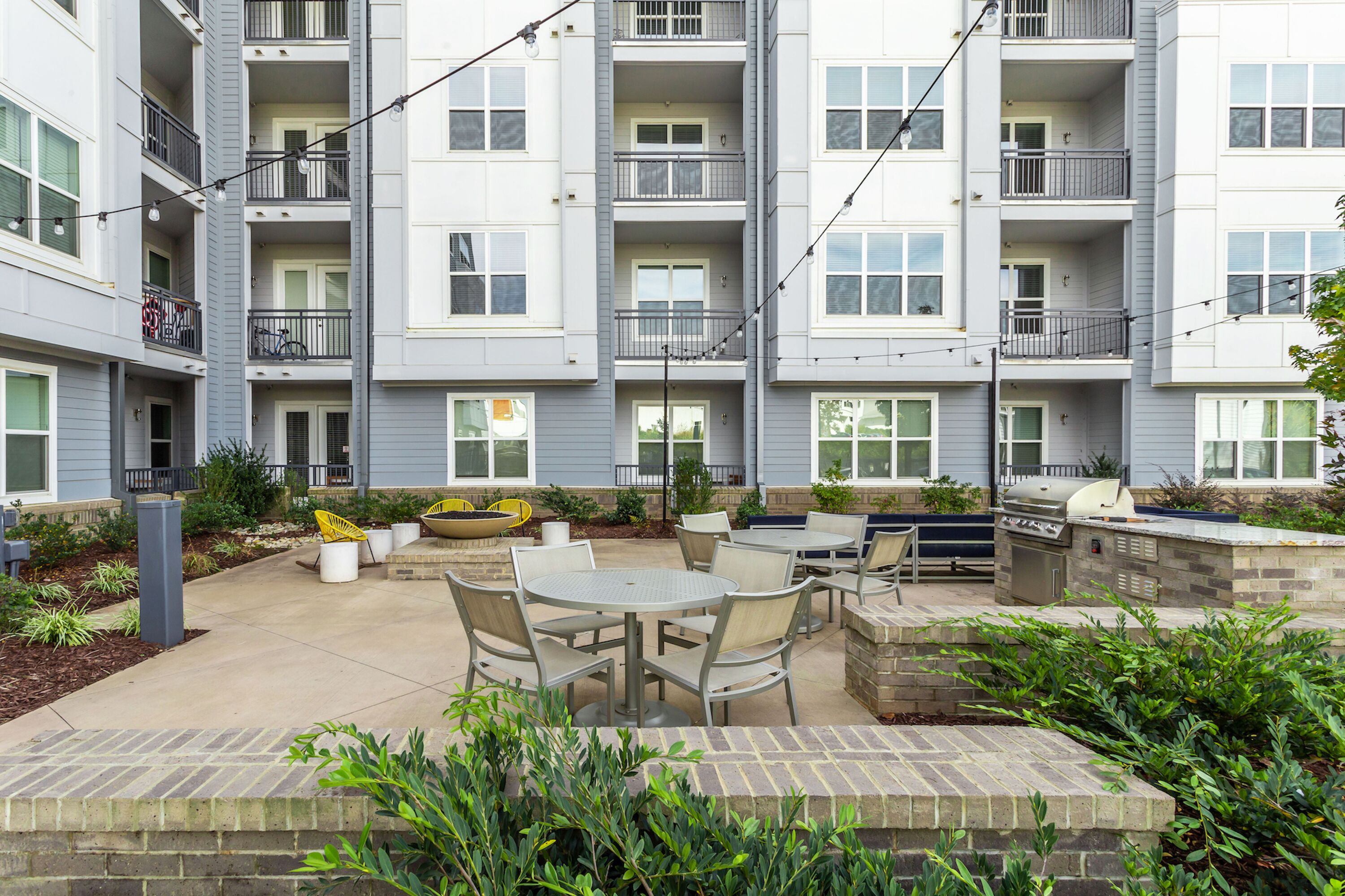 An outdoor patio area with multiple tables and chairs, a barbecue grill, and a small garden.