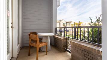 Un balcon avec une chaise en bois et une petite table, un mur en briques et une vue sur les maisons voisines.