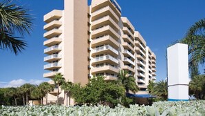 Un hotel de varios pisos con balcones, palmeras y un cielo azul despejado.