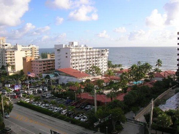 A coastal cityscape with a prominent hotel featuring multiple floors, a parking lot, and a view of the sea.