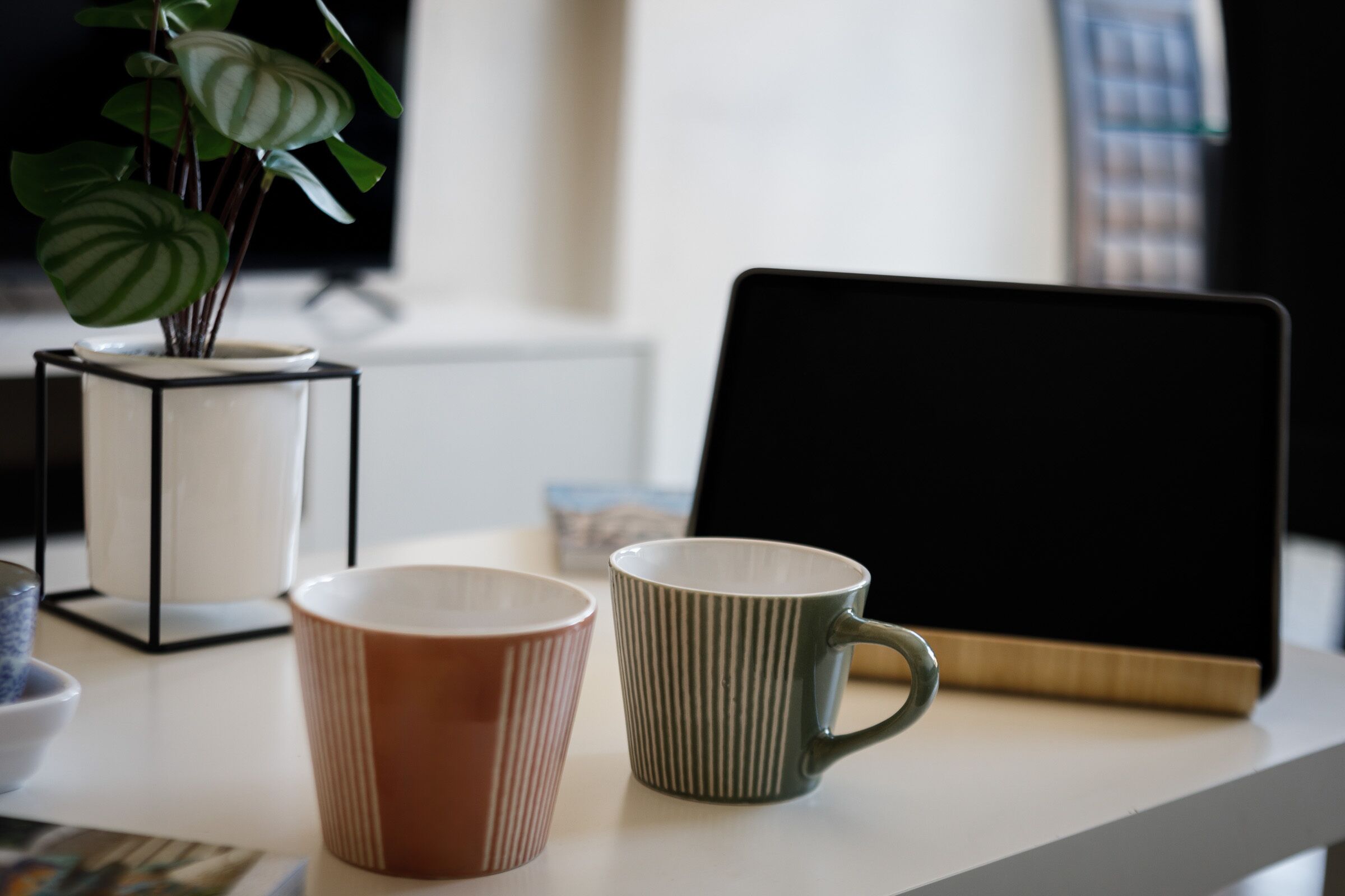A table with two mugs, a potted plant, and a tablet.