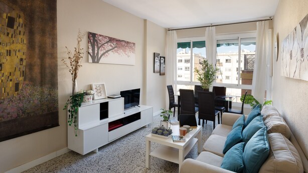 Ein modernes Wohnzimmer mit einer Couch, einem Couchtisch und einer TV-Bank. Es sind auch Sessel und ein Esstisch zu sehen.
