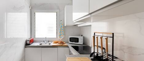Una cocina moderna con armarios blancos, un microondas, un tostador y una tabla de cortar de madera.