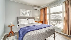 A bedroom with a bed, a nightstand, a window with curtains, and an air conditioner. - Cozy Home w/ Private Patio & Views, Hiking On-Site (Belleville)