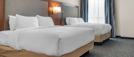 A hotel room with two beds, a headboard with a light fixture, a large window with curtains, and a carpeted floor.