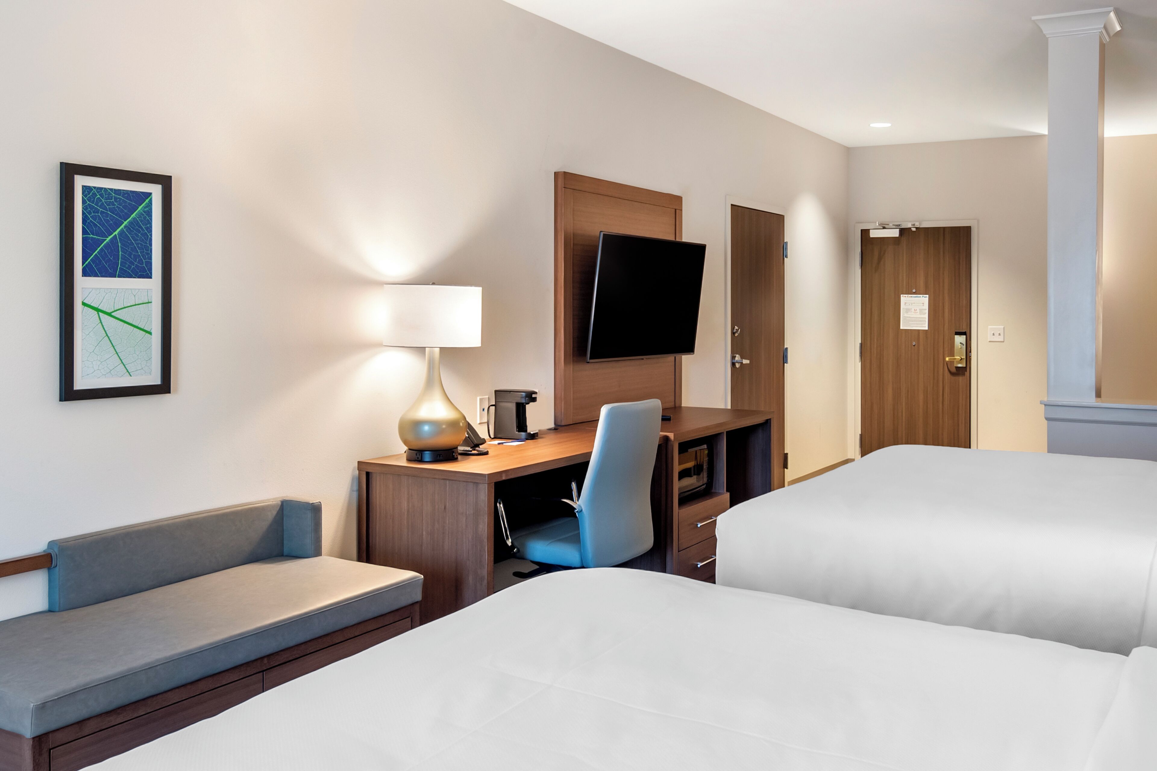 Una habitación de hotel con una cama, un escritorio con silla, un televisor y un cuadro en la pared.