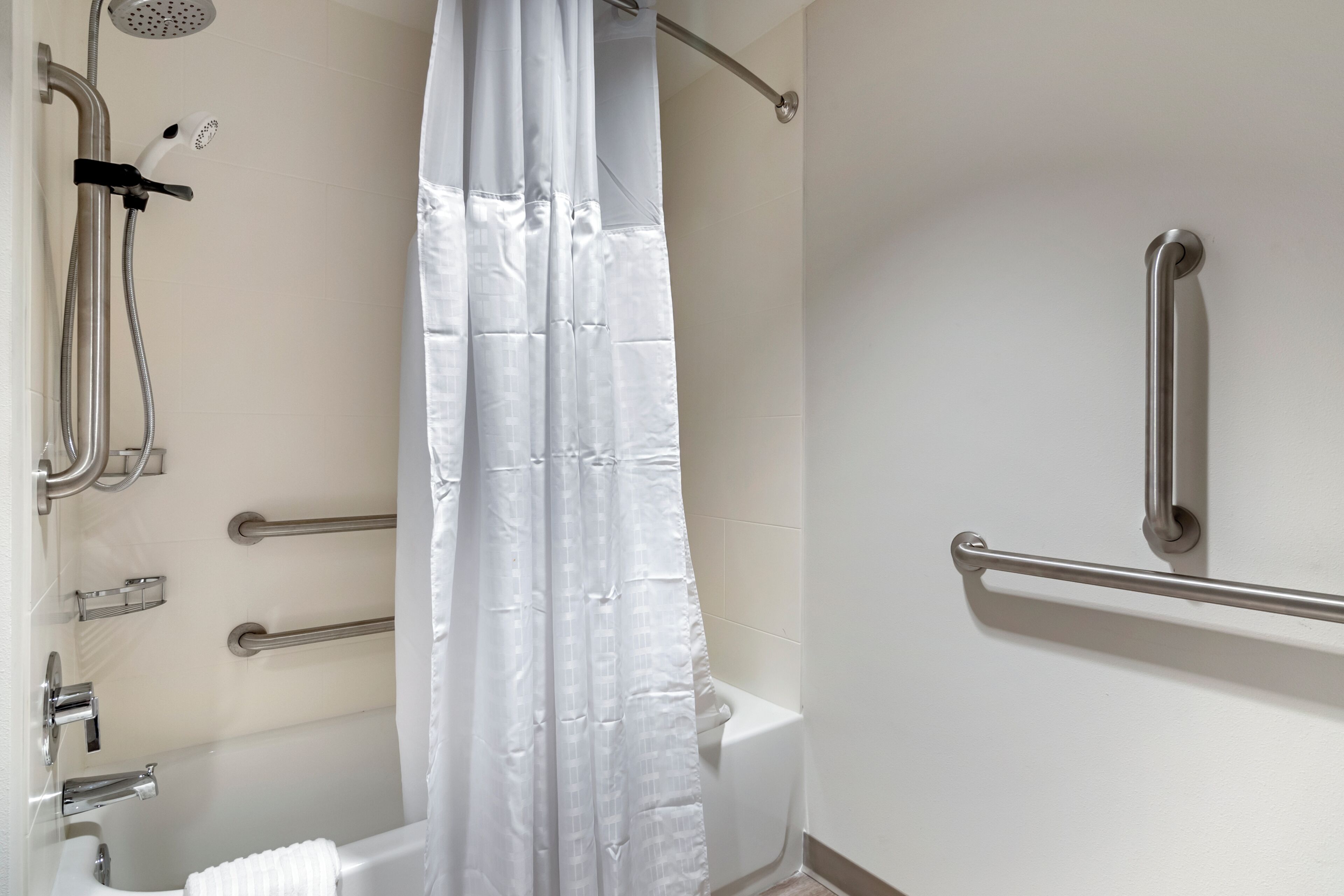 Un baño con ducha, barras de apoyo, bañera y retrete.
