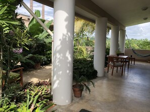 Un espace extérieur abrité, équipé d’une table et de chaises, entouré de plantes en pot et agrémenté d’un hamac.