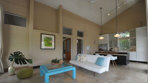 A modern living room with a white sofa, blue coffee table, and a large window. - Your home away from home on the Farm, 4 Casitas Bed n Breakfast - Casita 1 (Cabo Rojo)