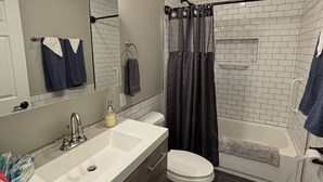 Een moderne badkamer met een witte wastafel, een donkere badkamerkast, een toilet en een bad met douchegordijn.
