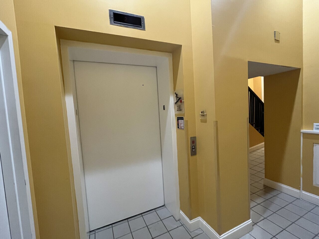 A hallway with a white door, yellow walls, and a tiled floor.