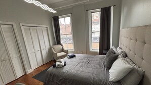 Une chambre d’hôtel avec un grand lit, une chaise et une vue sur la ville par les fenêtres.