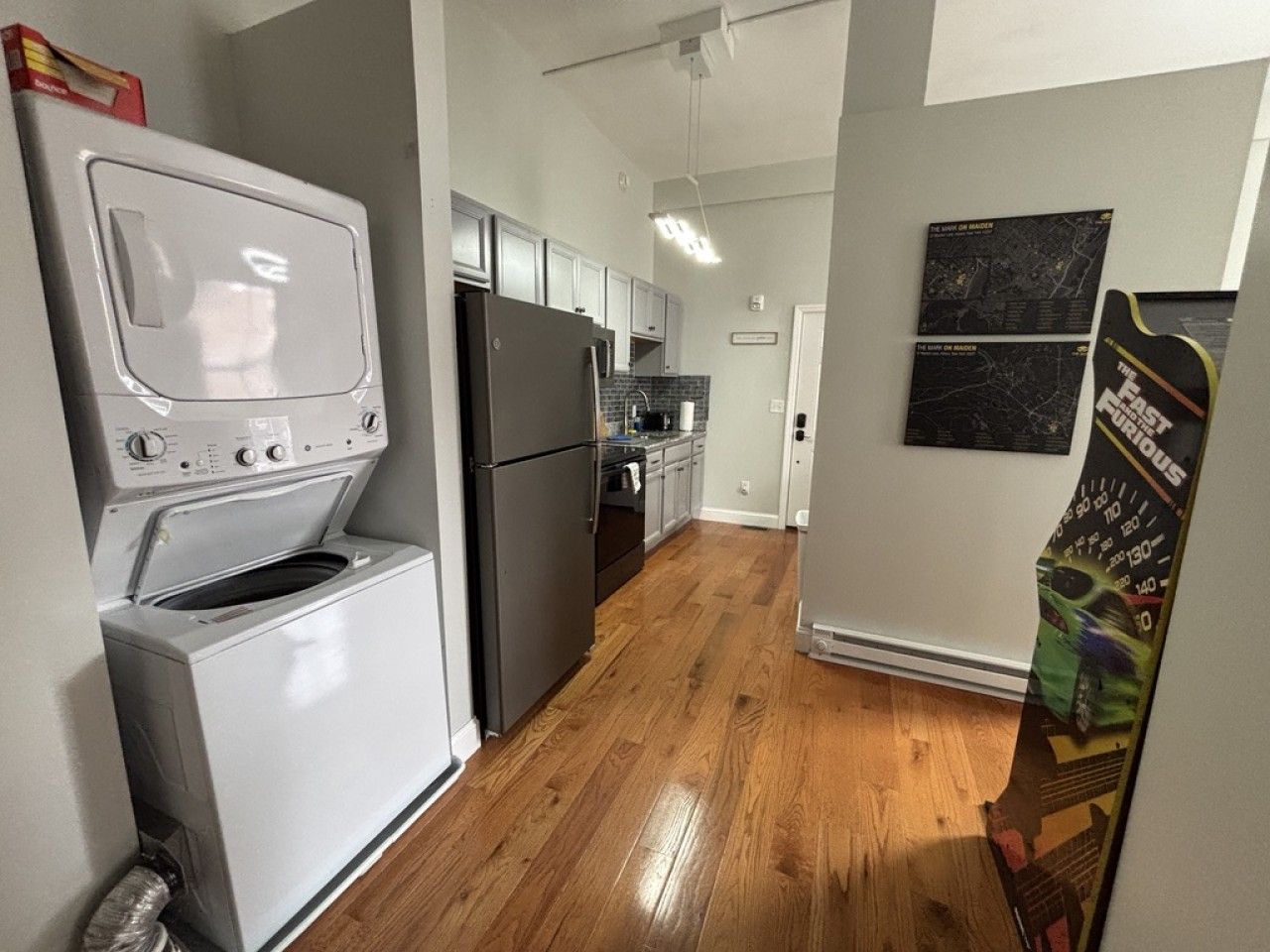 A kitchen with a washer and dryer, wooden flooring, and a poster on the wall.
