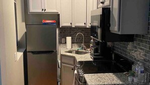Cocina compacta con armarios blancos, refrigerador de acero inoxidable, microondas y pileta.