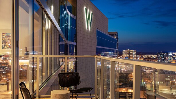 A modern building with a prominent 'W' logo, a glass balcony with a metal railing, and two black chairs. - W Nashville (Nashville)