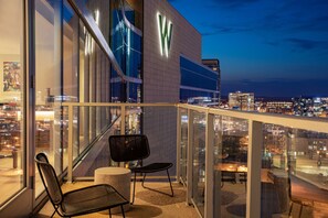 A balcony with a glass railing, two chairs, and a round table, overlooking a cityscape at dusk. - W Nashville (Nashville)