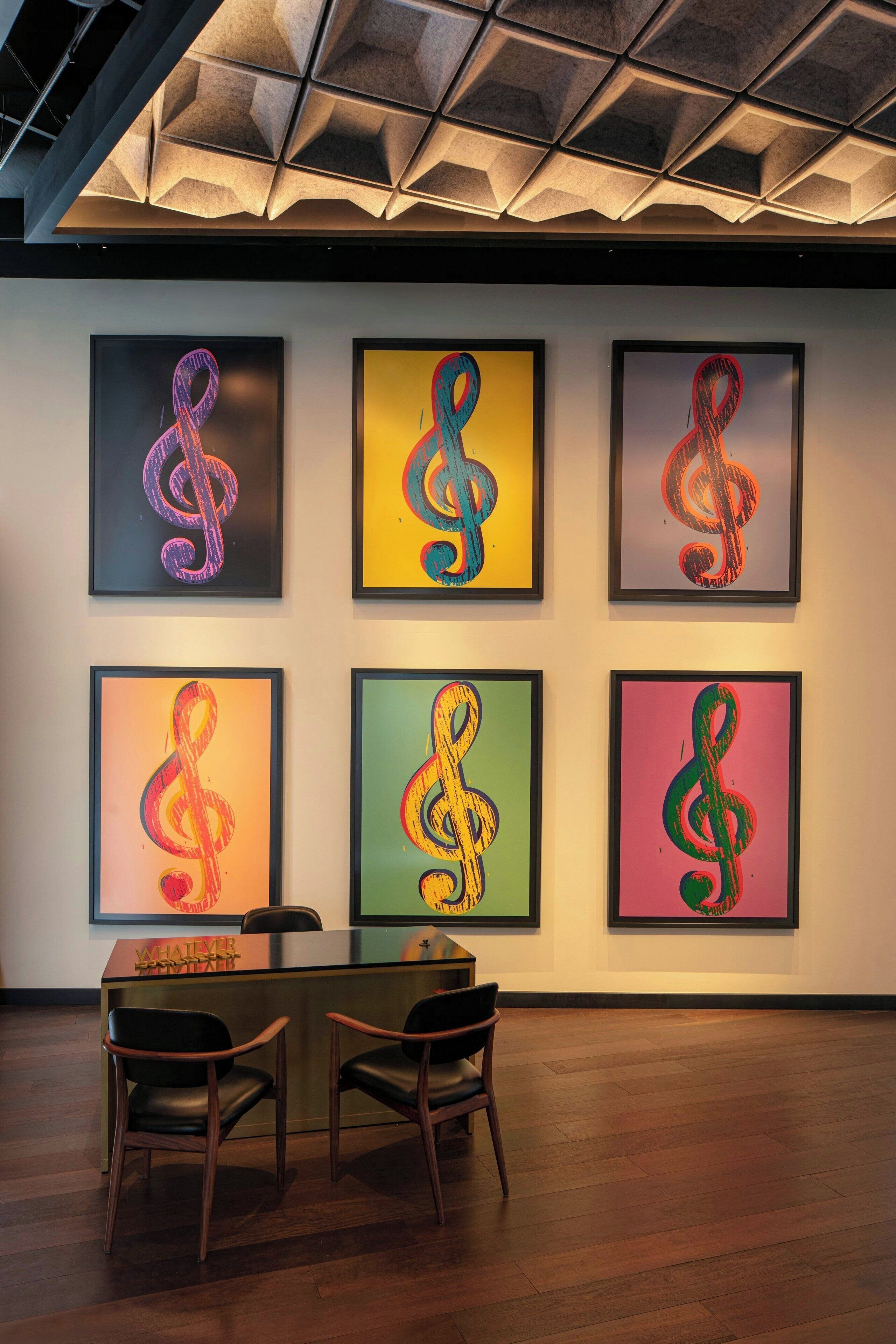 Eine Galerie mit sechs gerahmten Kunstwerken an der Wand, einem Empfangstisch und zwei Stühlen im Vordergrund.