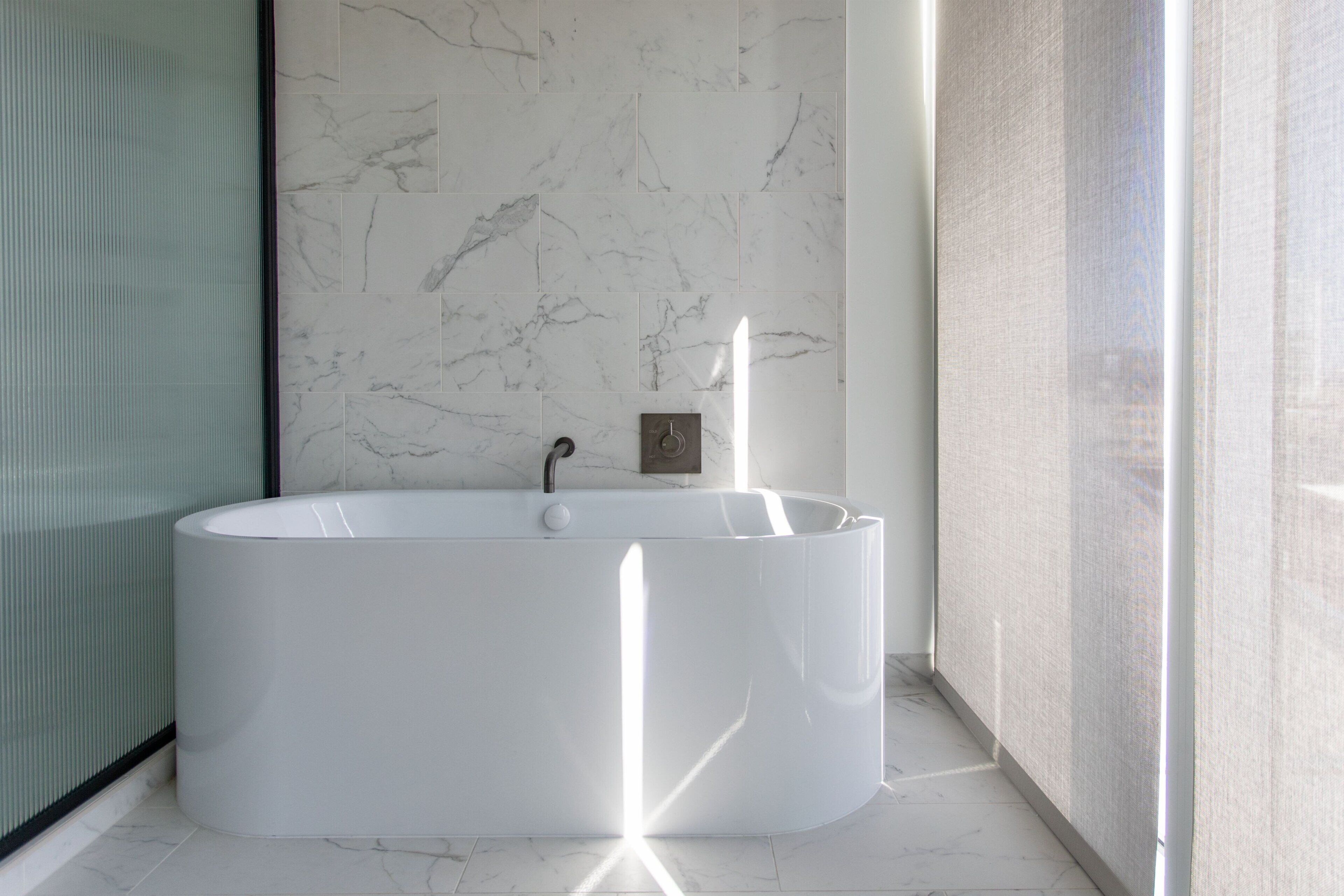 A modern bathroom with a freestanding bathtub, a glass shower enclosure, and a marble wall.