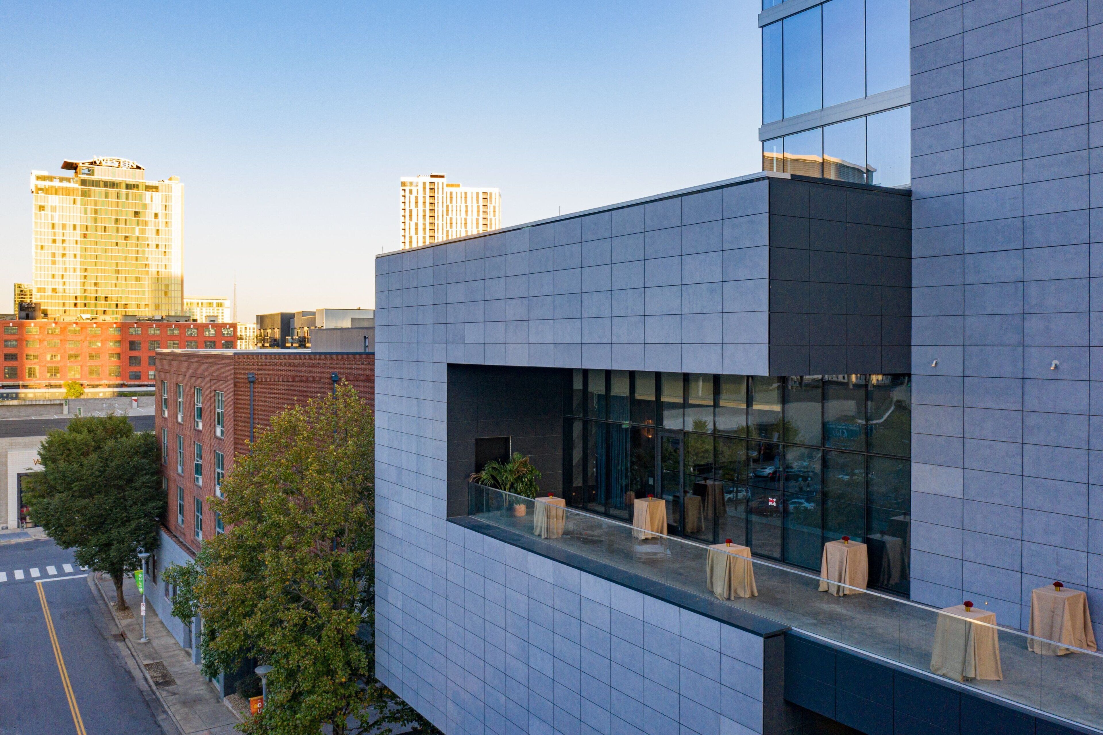 A modern building with a glass facade and a rooftop terrace with tables and chairs.