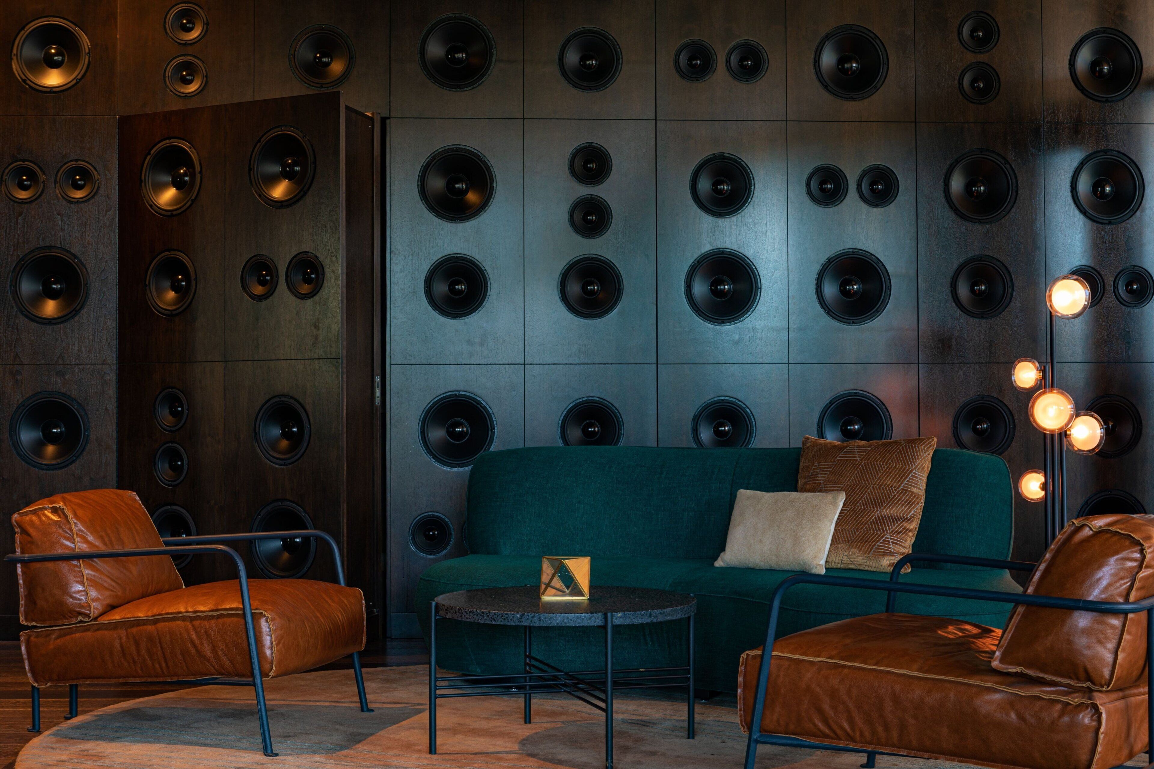 A room with a dark wood panel wall, leather armchairs, a teal sofa, and a small round table.