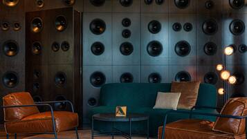 A room with a dark wood panel wall, leather armchairs, a teal sofa, and a small round table.