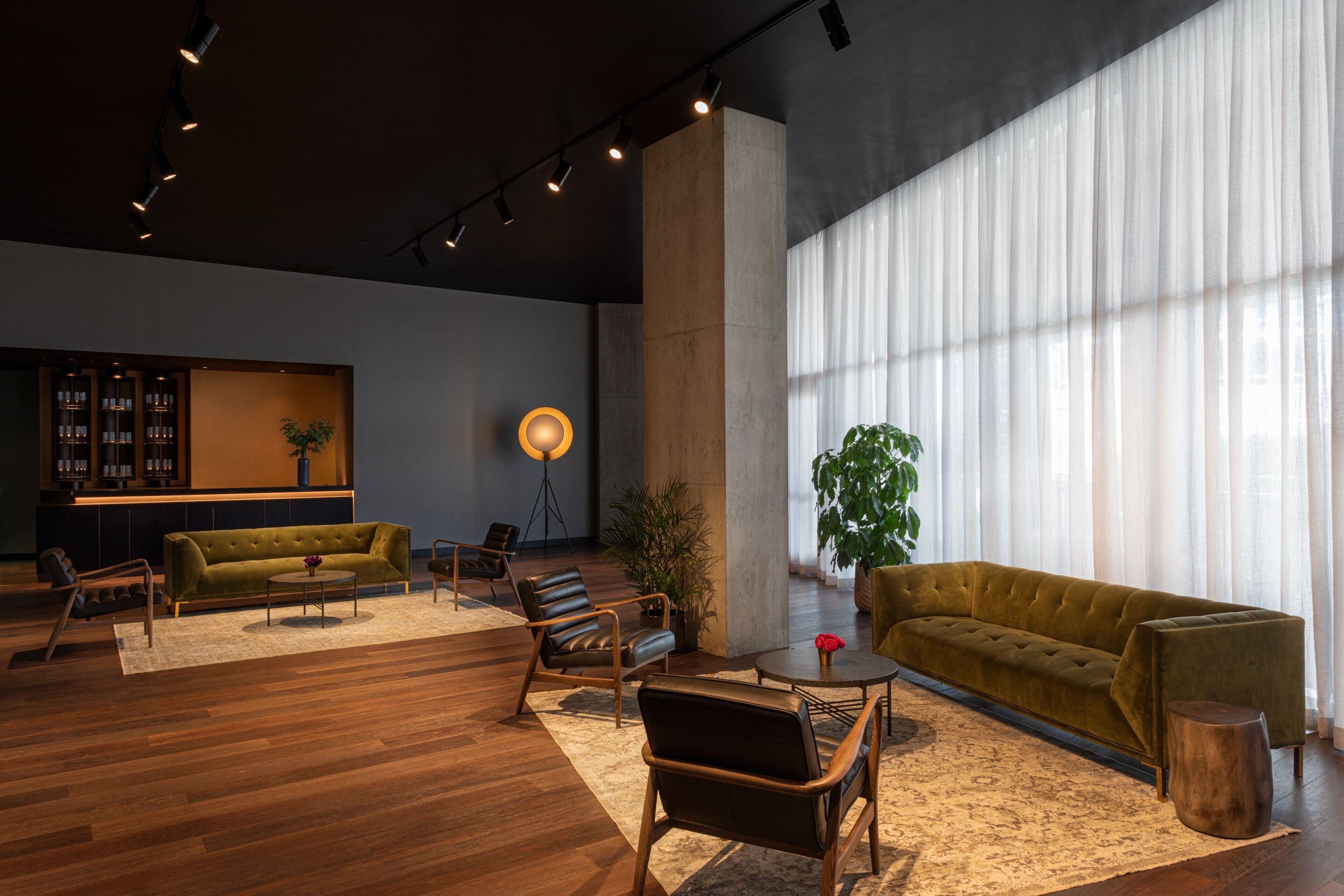 A modern living room with a large window, a sofa, chairs, a coffee table, and a bookshelf.