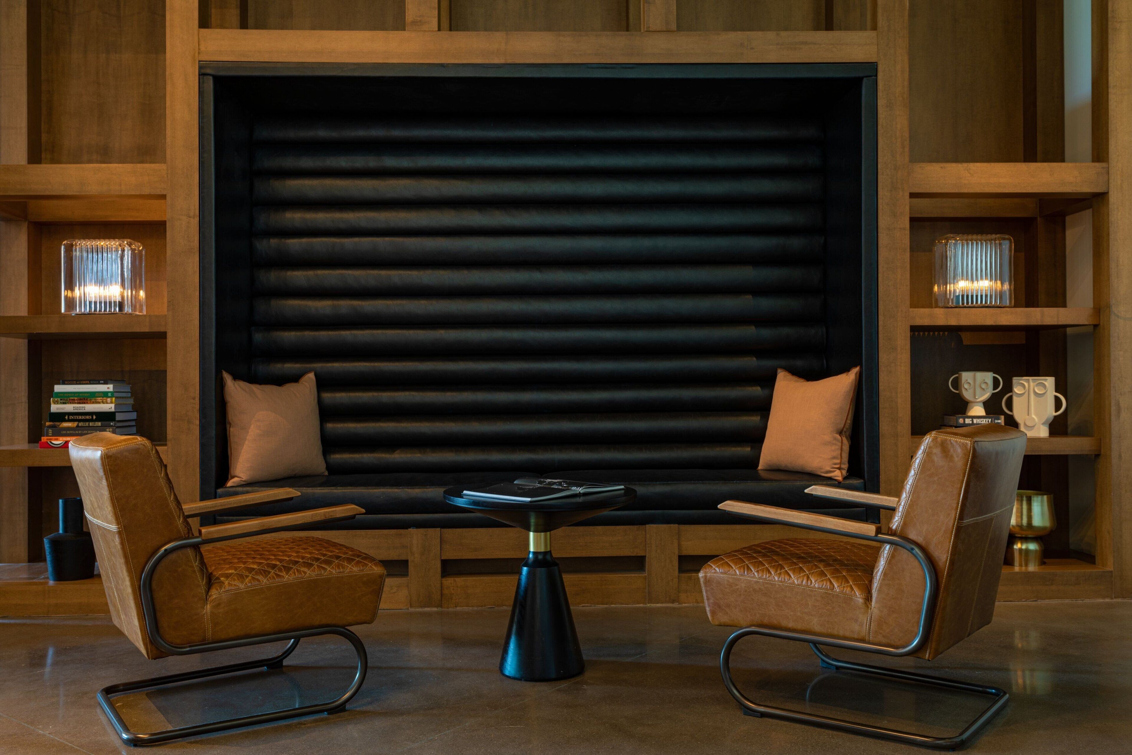 A modern lounge area with leather armchairs, a central coffee table, and a large black backdrop.