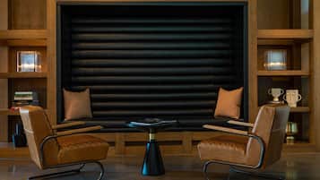 A modern lounge area with leather armchairs, a central coffee table, and a large black backdrop.