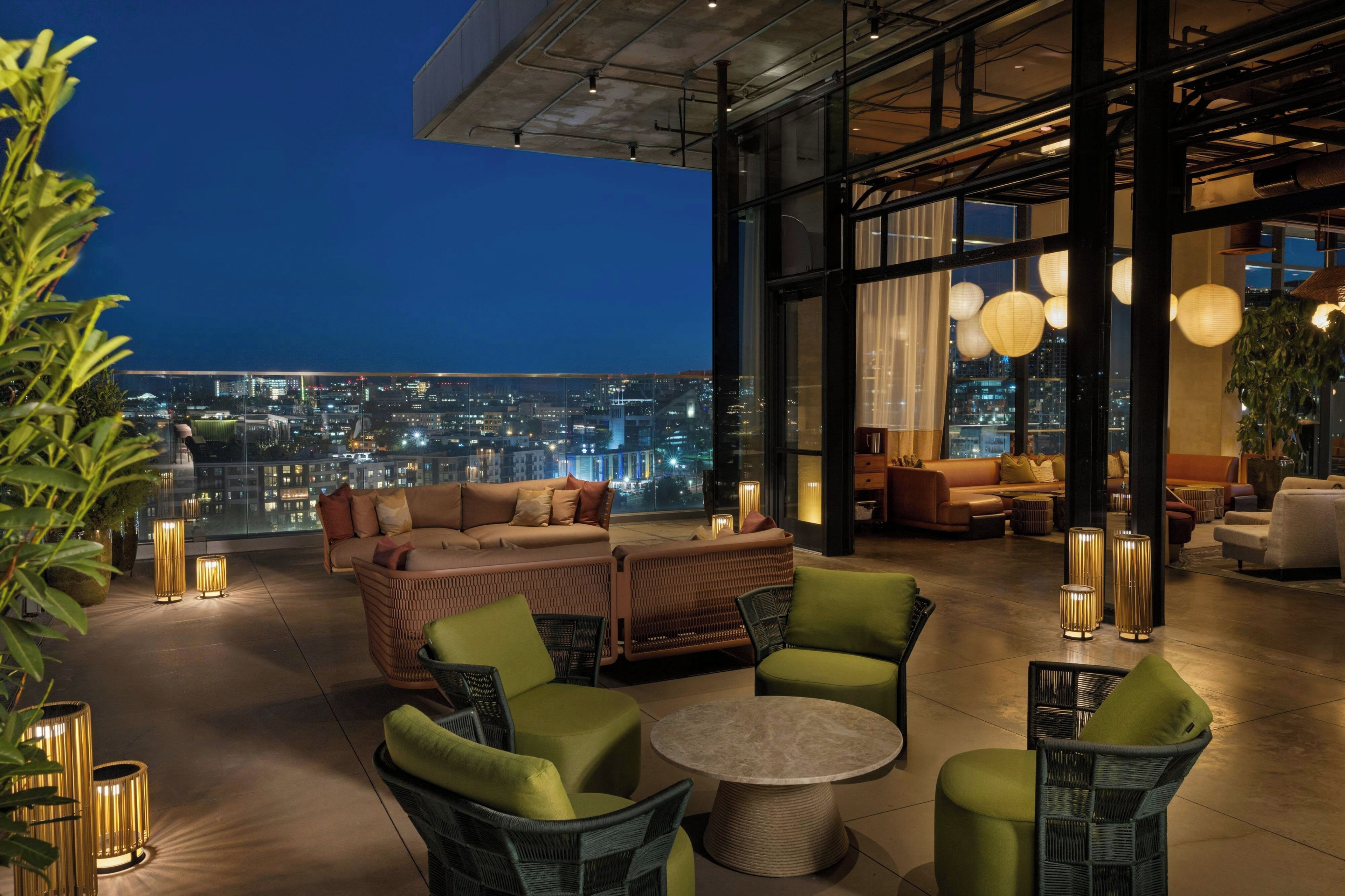 A rooftop lounge with a city view, furnished with sofas, chairs, and a round table.
