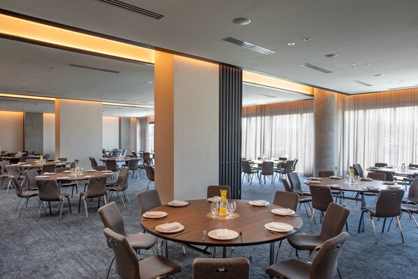 A conference room with round tables, chairs, and a large window with curtains.