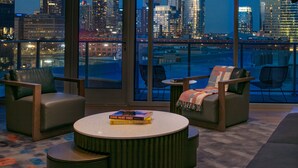 A modern hotel room with a large window offering a city view, two leather armchairs, a round coffee table, and a small bookshelf with travel books. - W Nashville (Nashville)