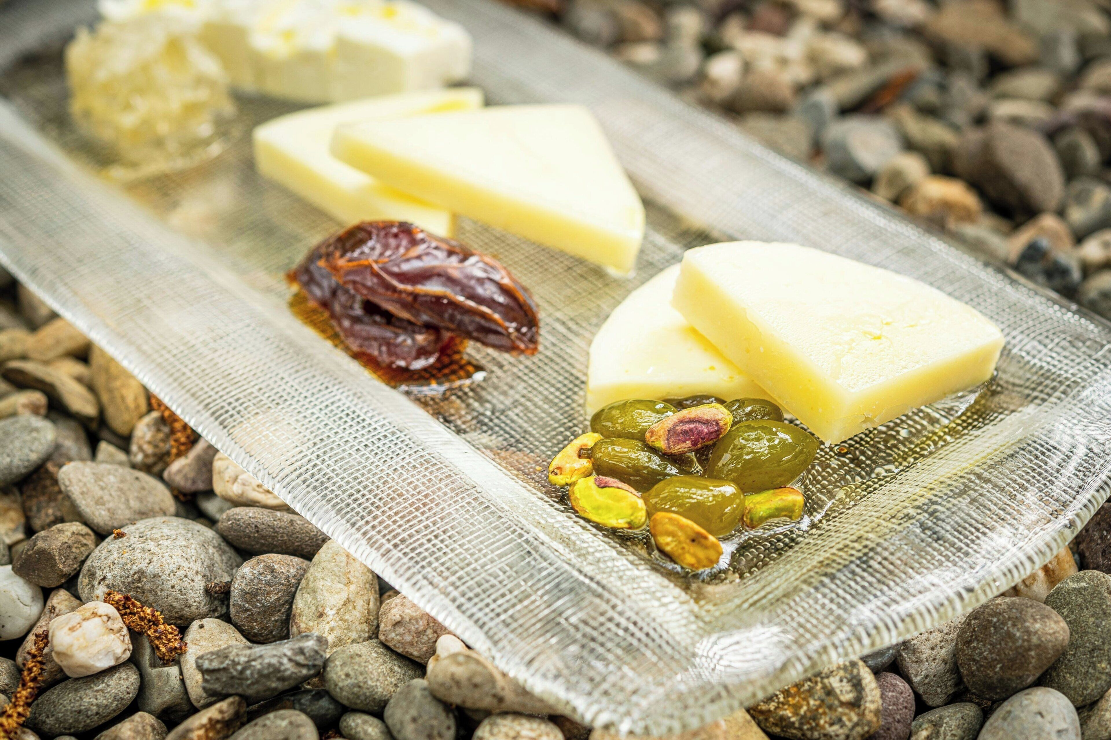 Una tabla de quesos con diferentes tipos de queso y frutas secas sobre un paño texturizado, sobre una capa de guijarros.