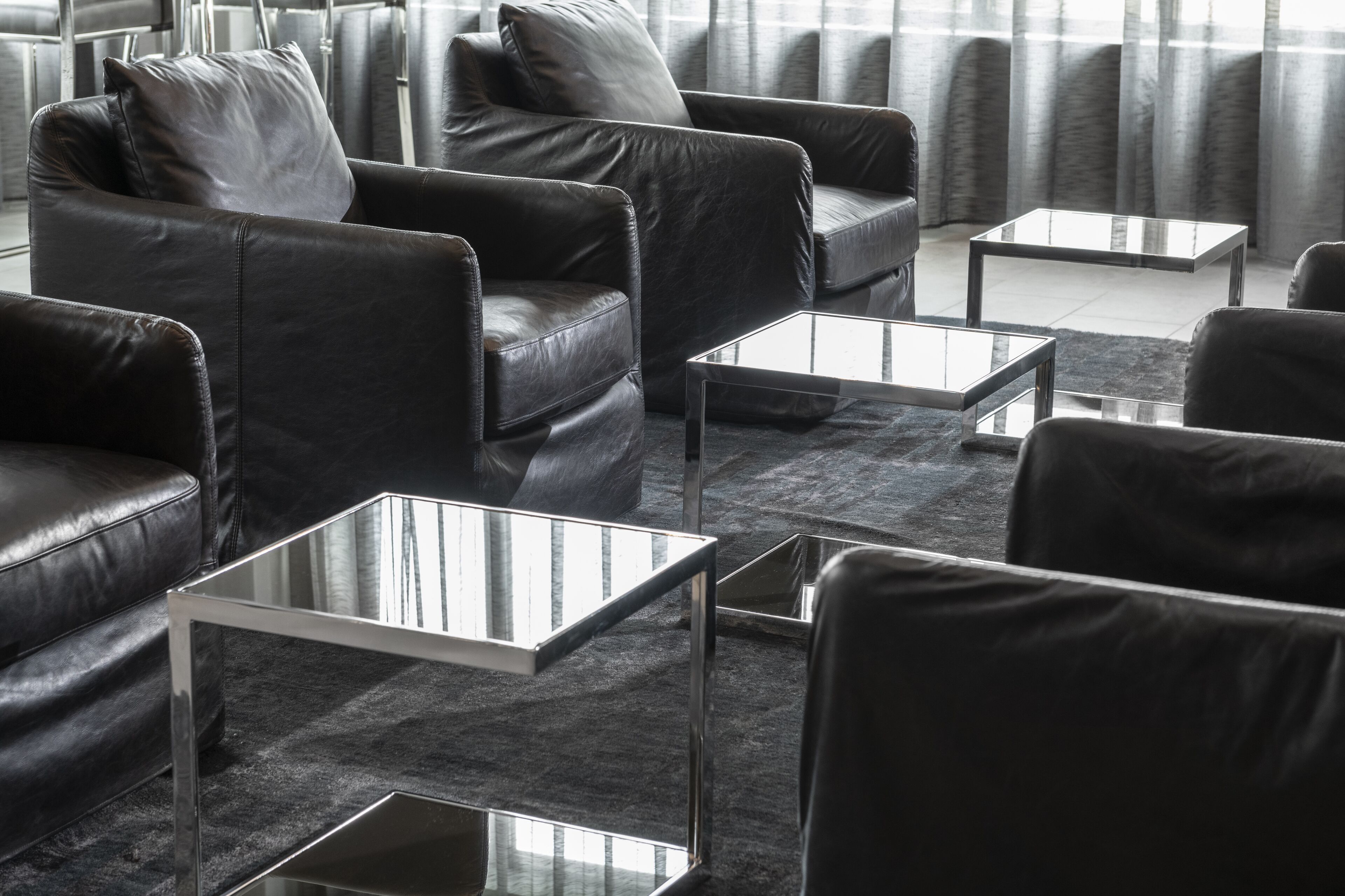 A modern living room with leather sofas and glass-top coffee tables arranged around a central area.