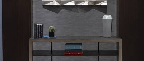 A modern interior with a wall-mounted geometric art piece, a console table with books and a small plant, and a tall white vase.