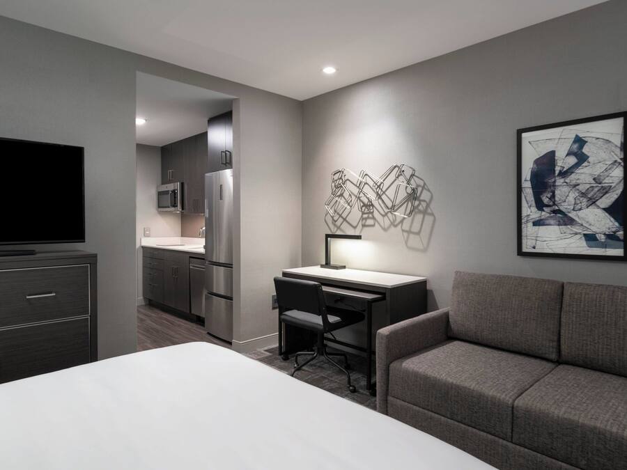 Una habitación de hotel moderna con una cama grande, un escritorio con una silla, un sofá, un televisor de pantalla plana, un microondas y un refrigerador.