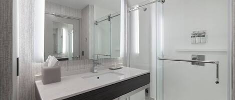A modern bathroom with a glass shower enclosure, a large mirror, and a white sink with a dark countertop.