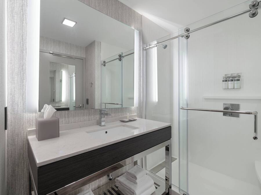 Un baño moderno con cabina de ducha de vidrio, un espejo grande y un lavamanos blanco sobre una encimera oscura.