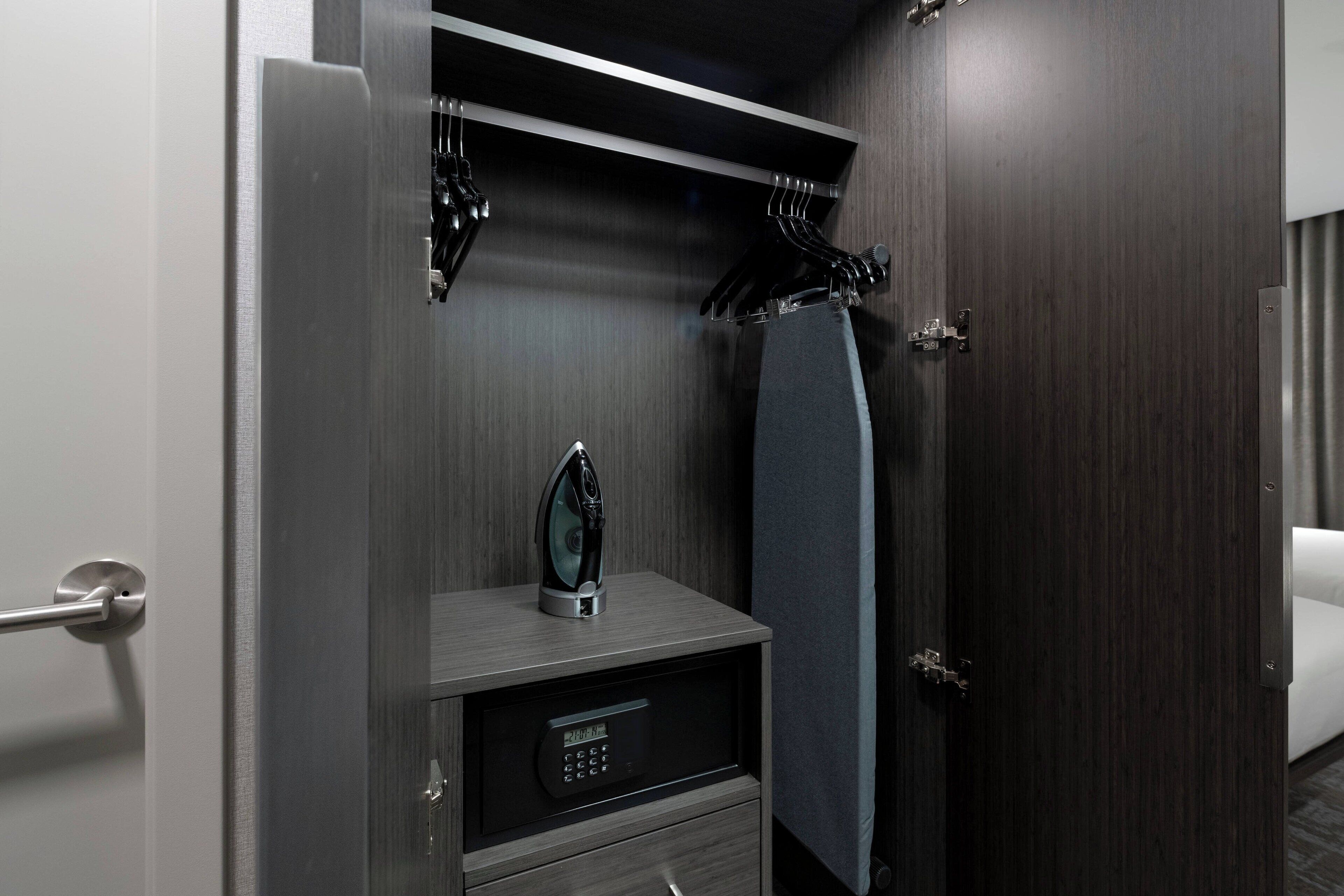 A hotel room with a dark wood door, a small bedside table with a digital lock, a towel hanging on the door, and a bed with a white cover.