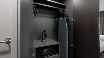 A hotel room with a dark wood door, a small bedside table with a digital lock, a towel hanging on the door, and a bed with a white cover.