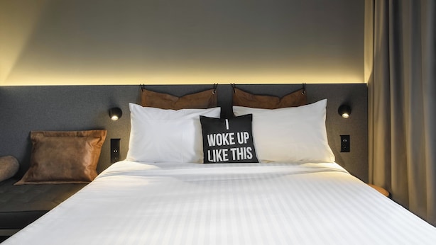 Una cama bien hecha con sábanas blancas y una almohada con el texto "I WOKE UP LIKE THIS".