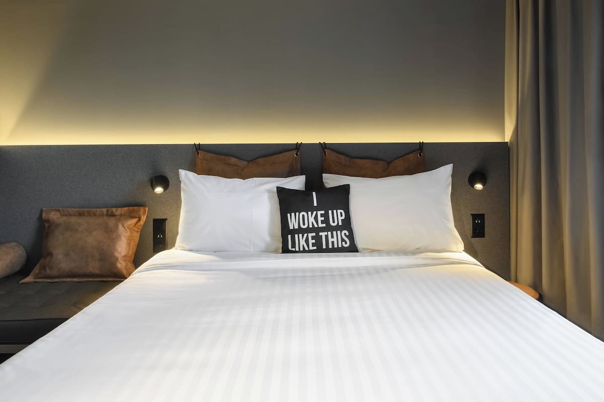 Cama bem arrumada com lençóis brancos e almofada com a inscrição 'I WOKE UP LIKE THIS'.