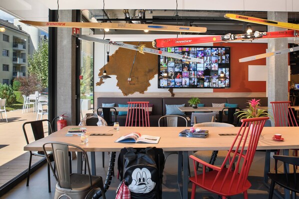 Un comedor moderno con una mesa grande, sillas rojas y vistas de la ciudad a través de amplias ventanas.